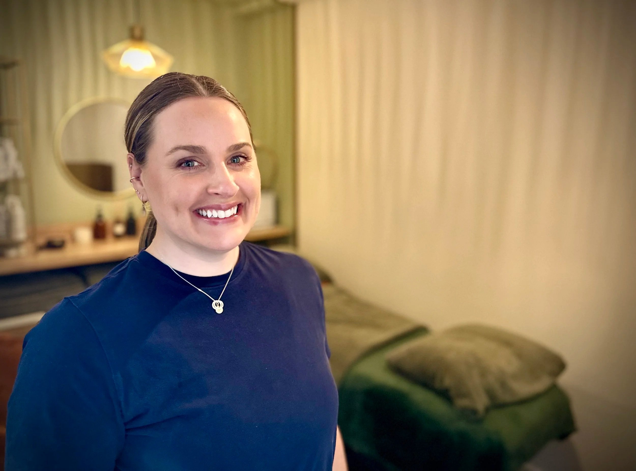 A beauty therapist stands in a warmly lit comfortable treatment room of Elvy Beauty of Thirsk, North Yorkshire, UK where customers can receive premium beauty, skin care and nail treatments including CACI synergy non-invasive treatment.