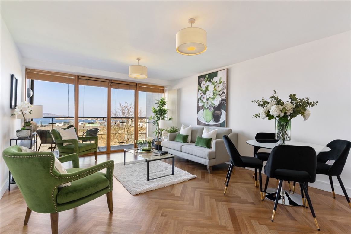 Living room with large windows, green and white furniture, a dining table with black chairs, and decorative flowers.