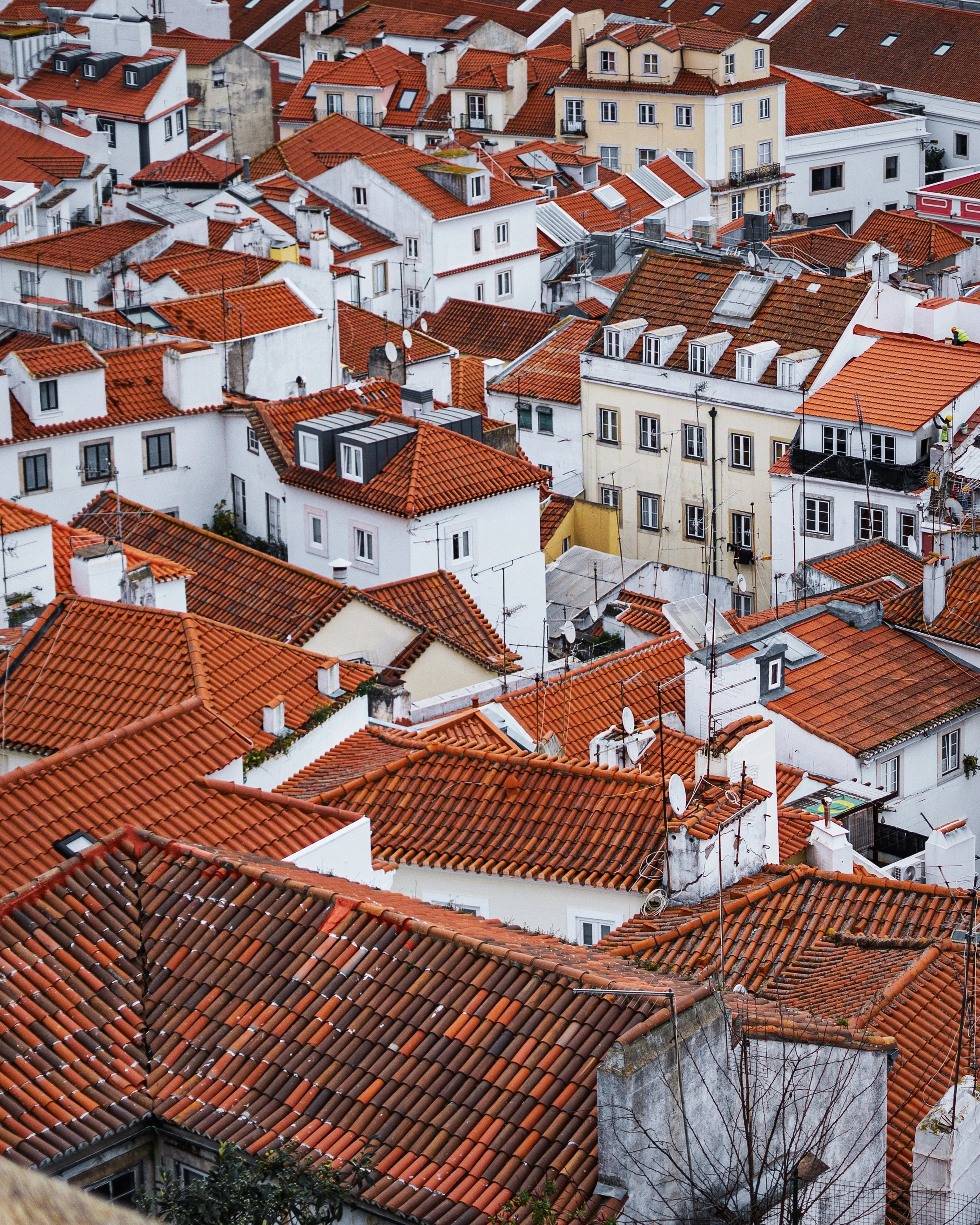 A dense cityscape with many white buildings and red-tiled roofs, some with skylights and chimneys, seen from above.