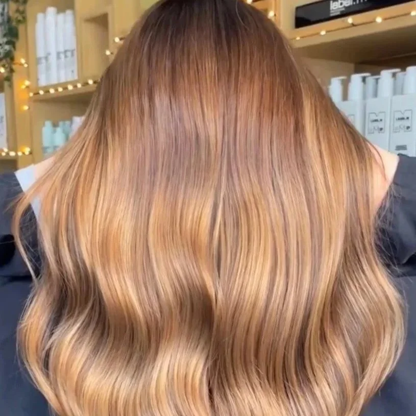 Back of a person with long, wavy, light brown to blonde hair in a salon setting.