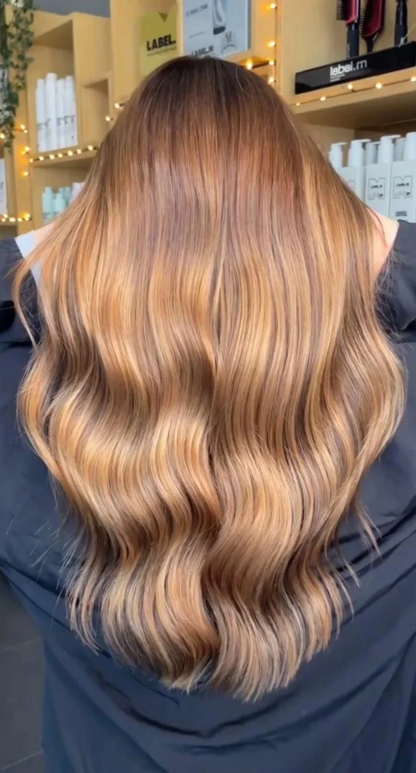 Back of a person with long, wavy, ombre hair transitioning from dark brown at the roots to blonde at the tips, in a salon setting.