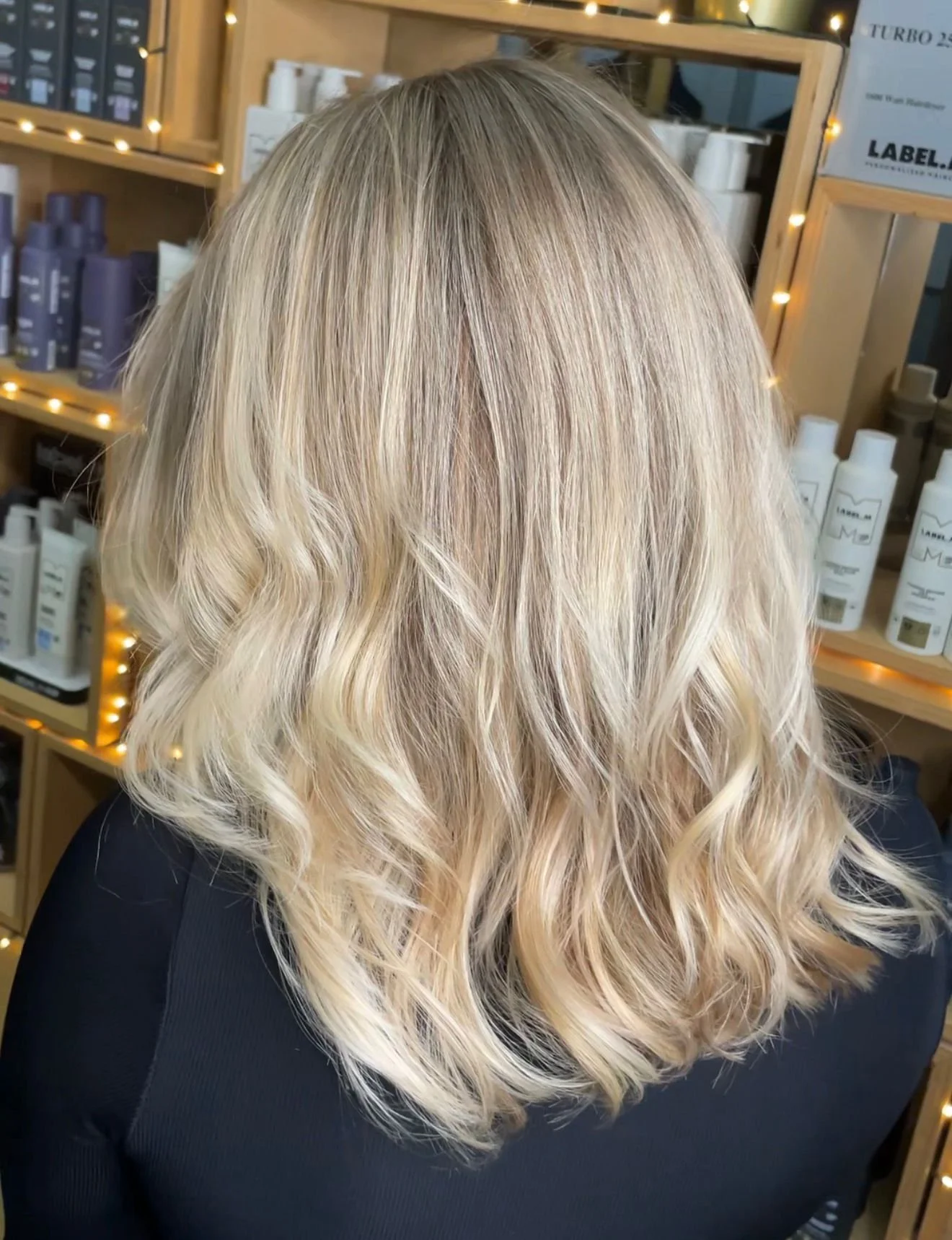 Blonde woman with shoulder-length wavy hair, seen from the back, in a hair salon.