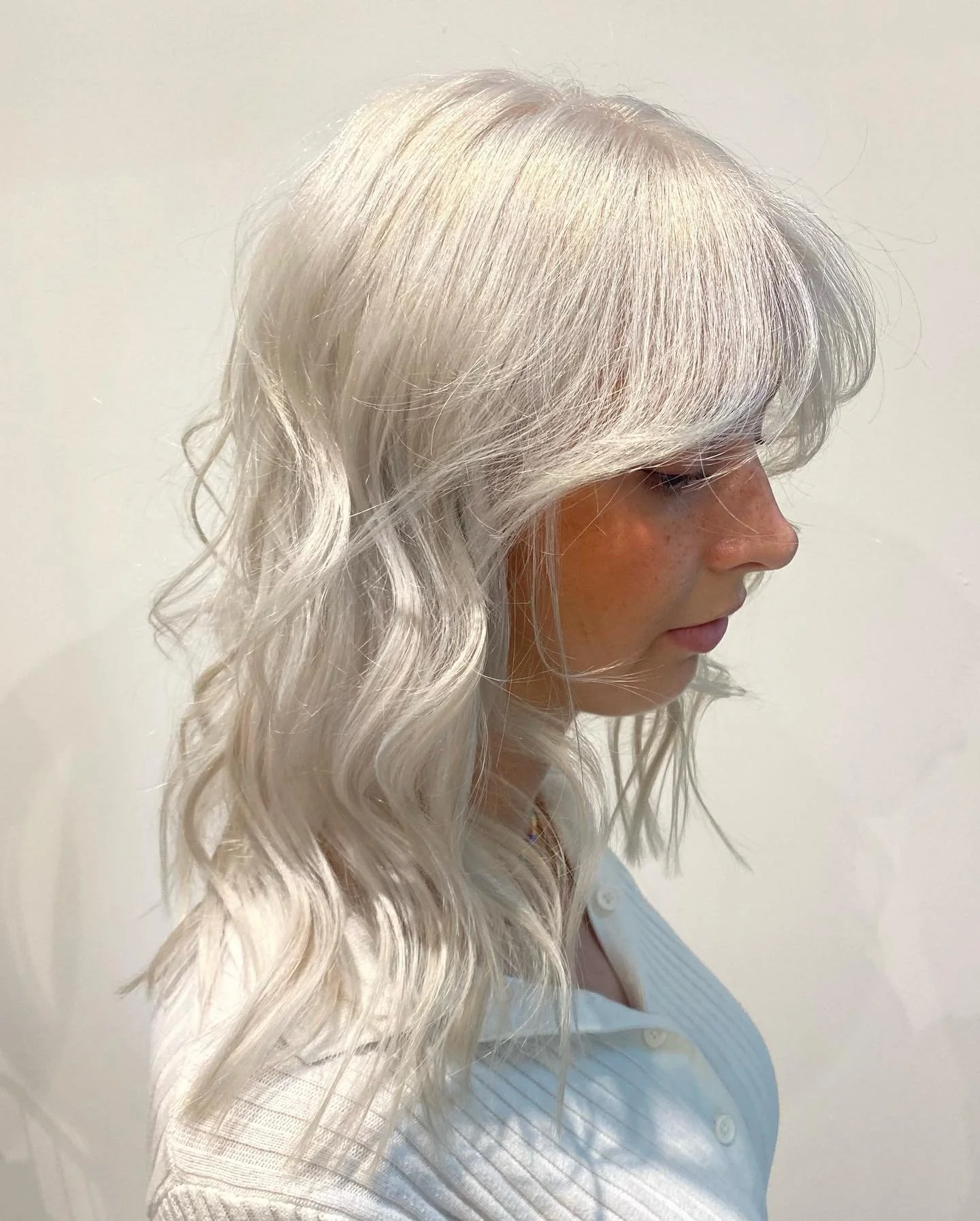 Side profile of a woman with long, wavy platinum blonde hair.