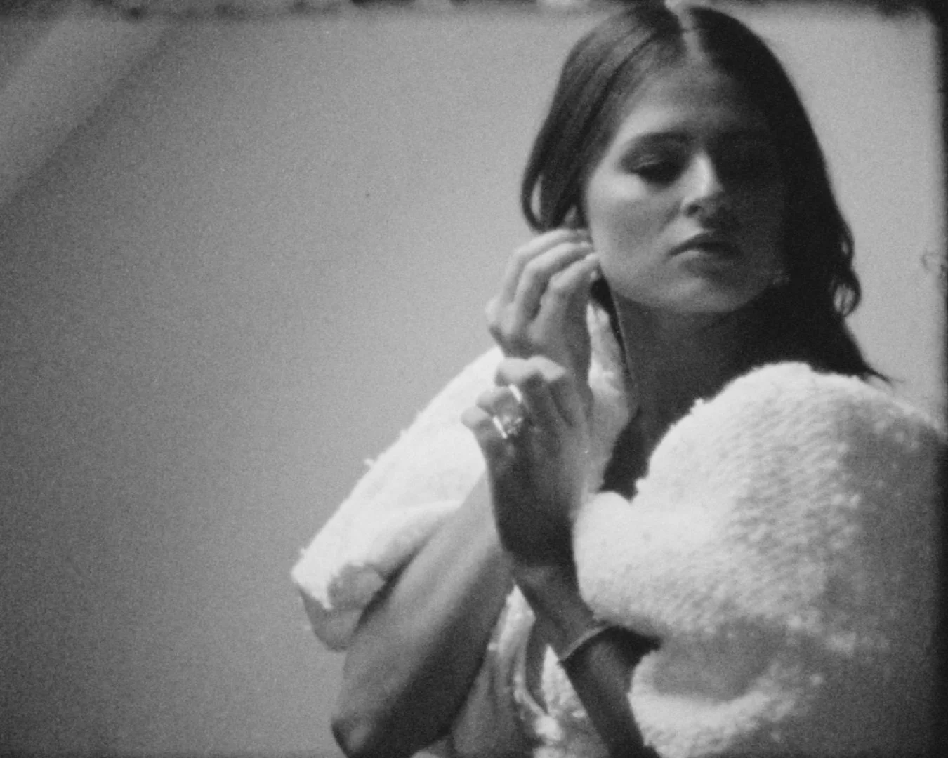 Black and white photo of a woman touching her ear and shoulder, looking to her left with a calm expression.