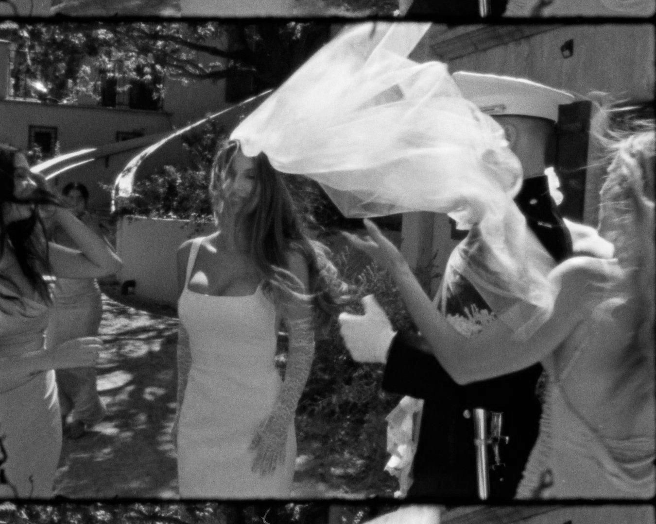 A group of women at an outdoor event, one woman is in a white dress with a veil, suggesting a wedding or celebration.
