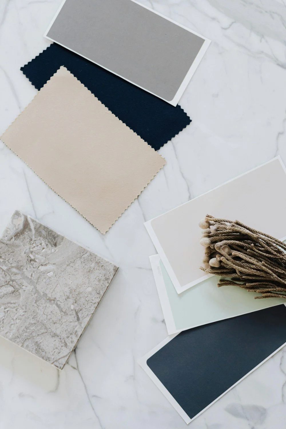 Sample swatches of various fabric, tile, and paint colors arranged on a marble surface, with some fabric samples tied with a string.