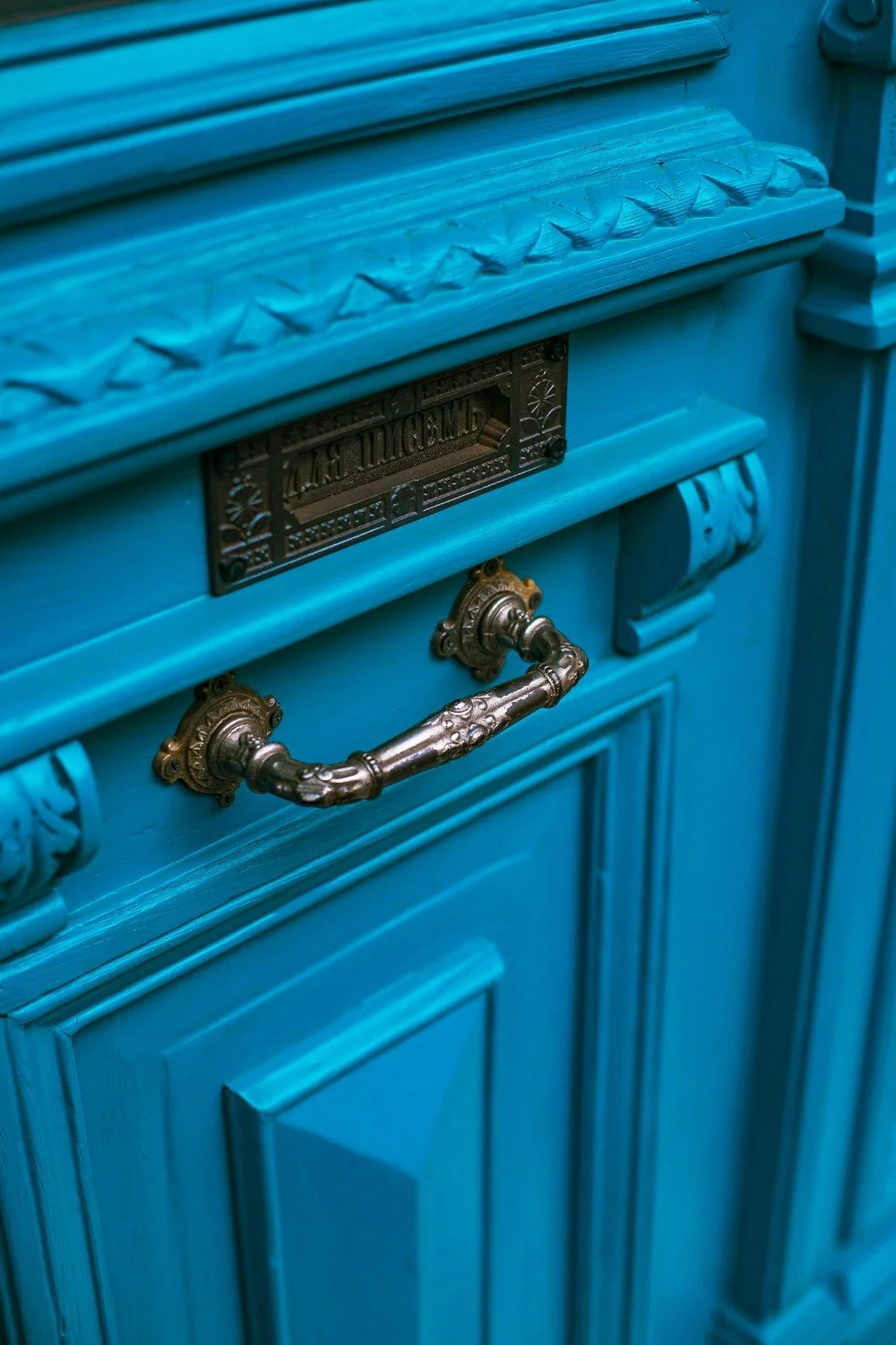 Close-up of a vintage blue cabinet with ornate bronze handles and decorative details, featuring a metal nameplate.