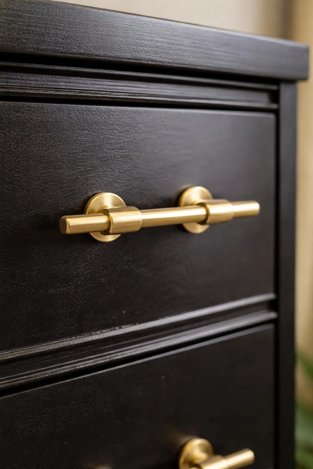 Close-up of a black wooden drawer with three gold-colored metallic handles.