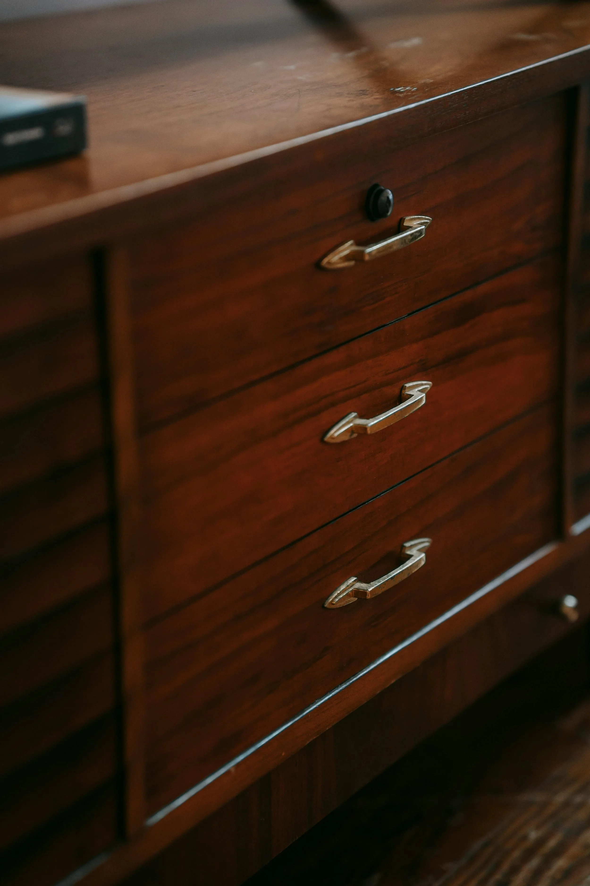Close-up of a wooden dresser with three drawers, each with metallic handles. Part of a black object is visible on the top left corner.