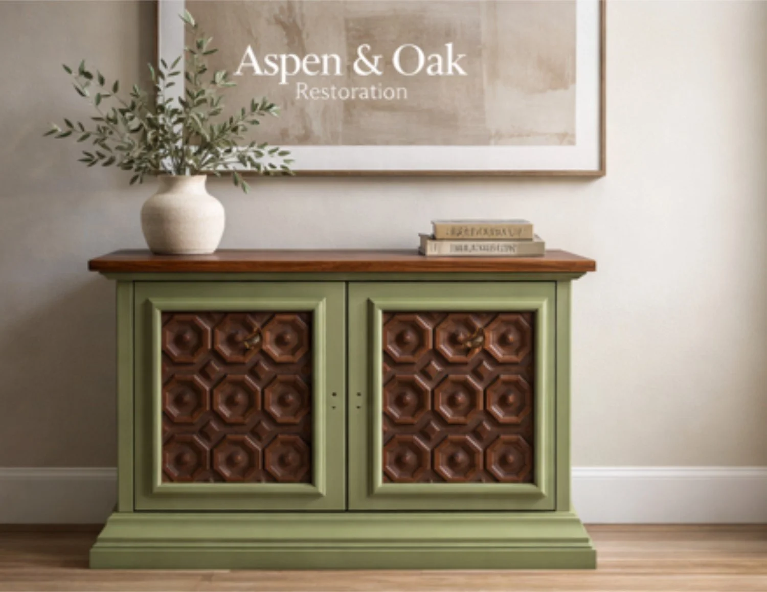 A green and brown sideboard with decorative panels on the doors, topped with a beige vase containing green leaves and a small stack of books, placed in front of a wall with a framed print that reads "Aspen & Oak Restoration."