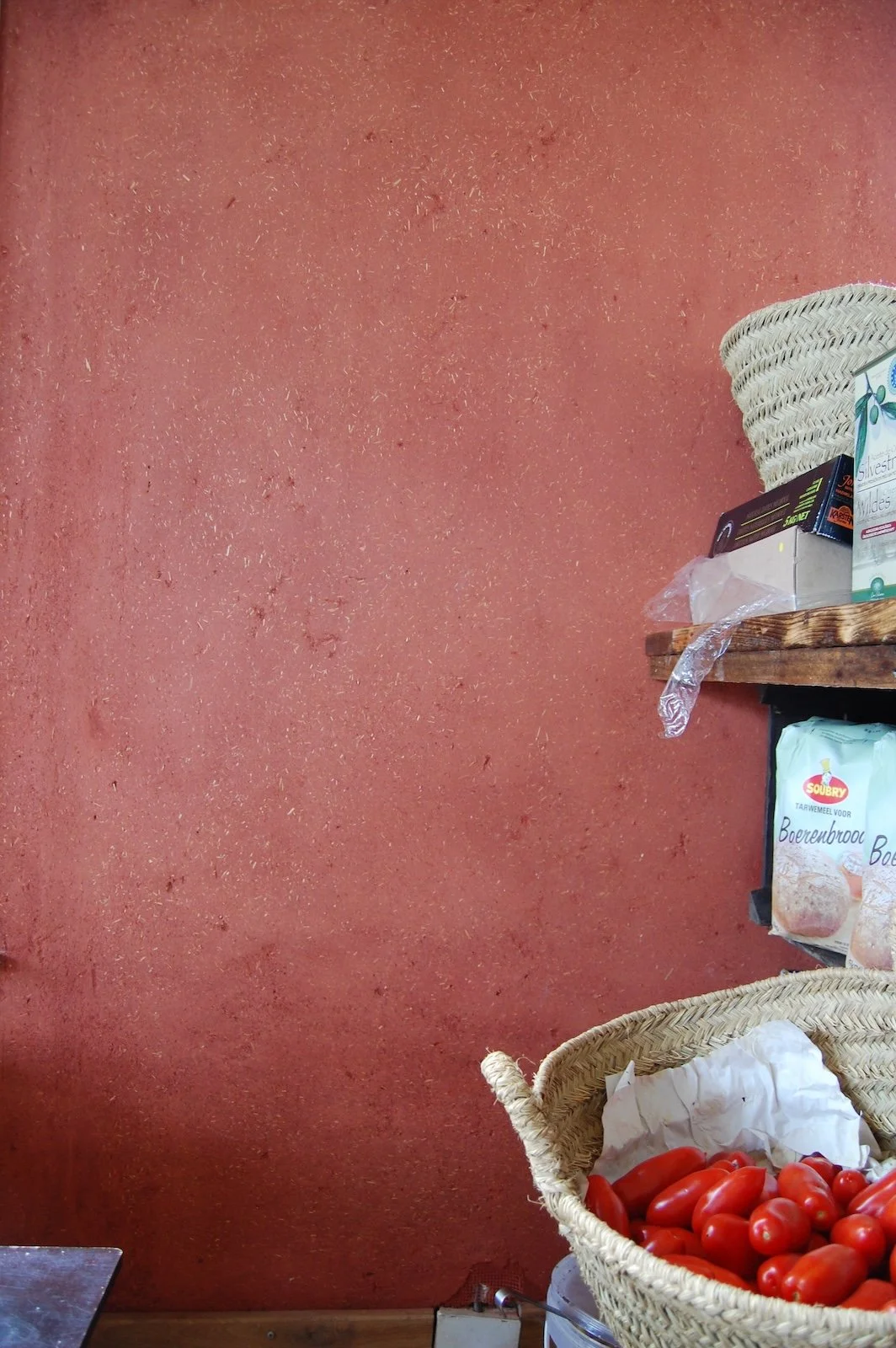 Detailfoto van leemstuc wand met zichtbare strovezels en warme rode pigmenten