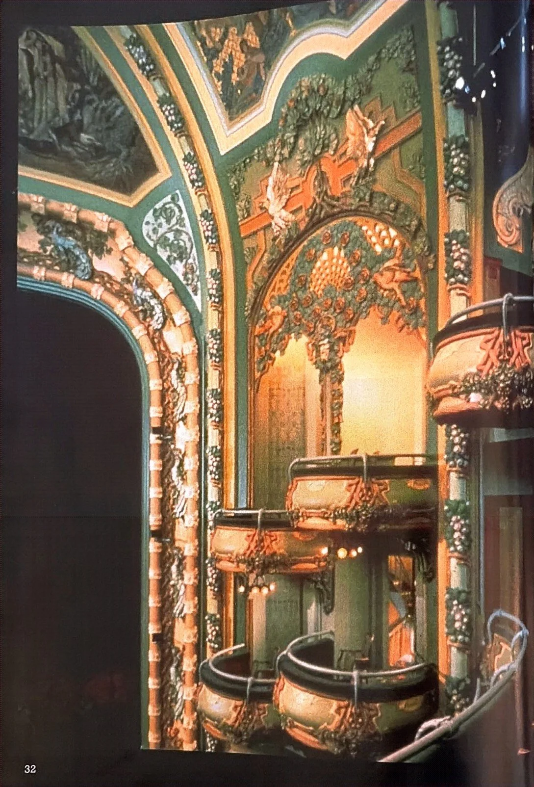 Ornate theater interior with elaborate decorative moldings, floral motifs, painted ceiling, and tiered seating.