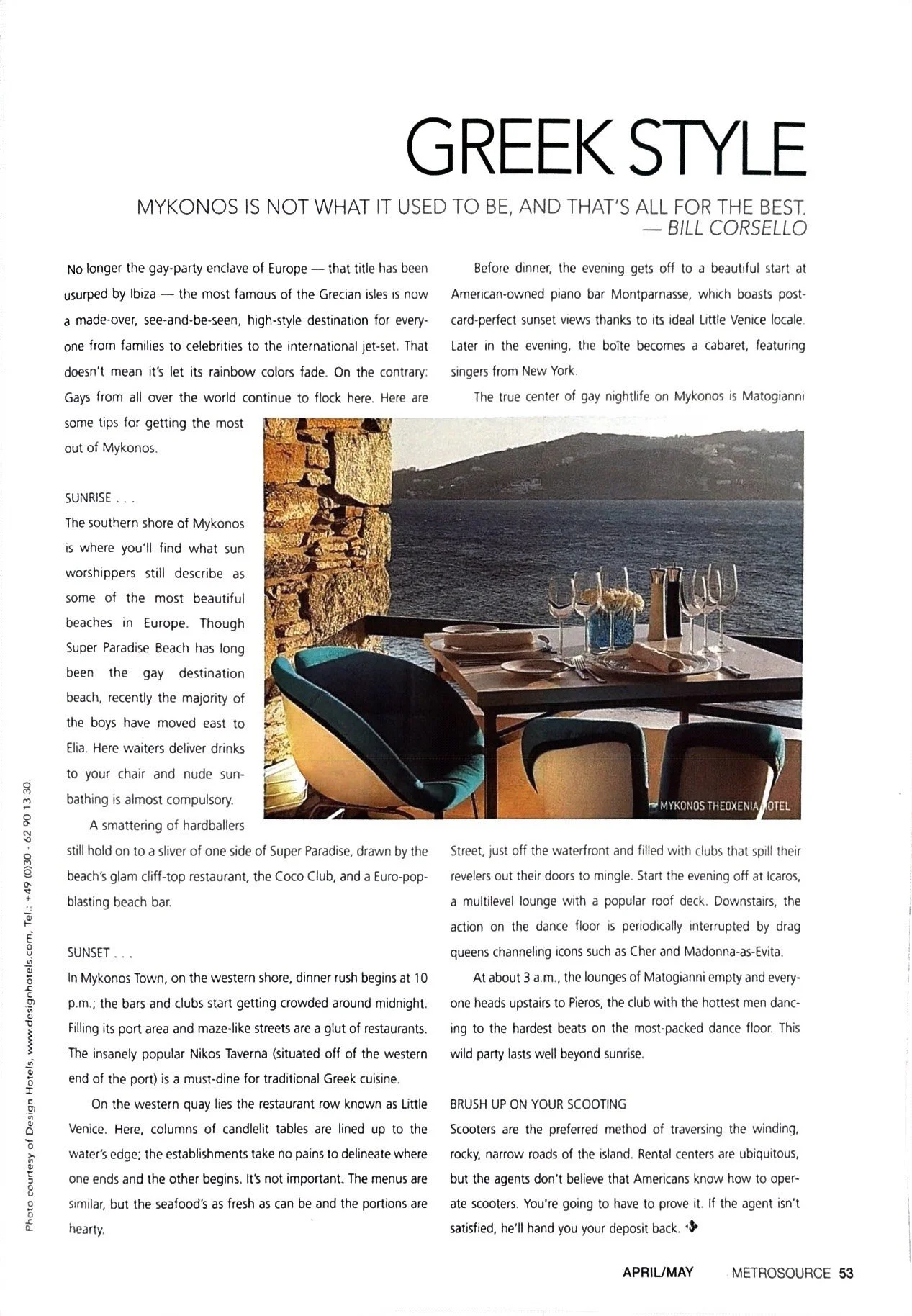 A restaurant table set with wine glasses, plates, and a vase of flowers, overlooking a body of water at sunset in Mykonos.