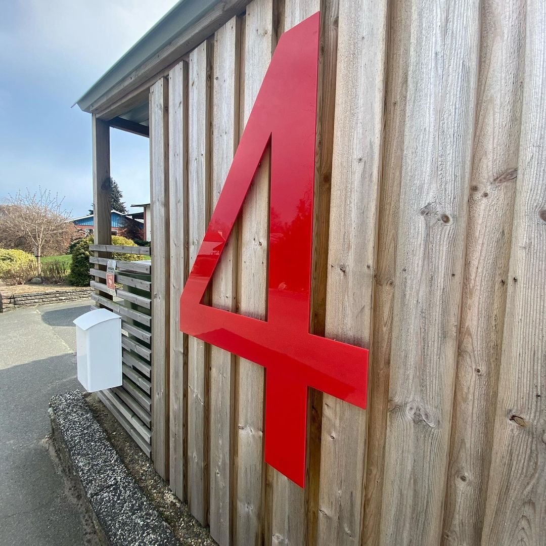 Husnummer 4 i pulverlackerat röd rostfritt metall på träpanel