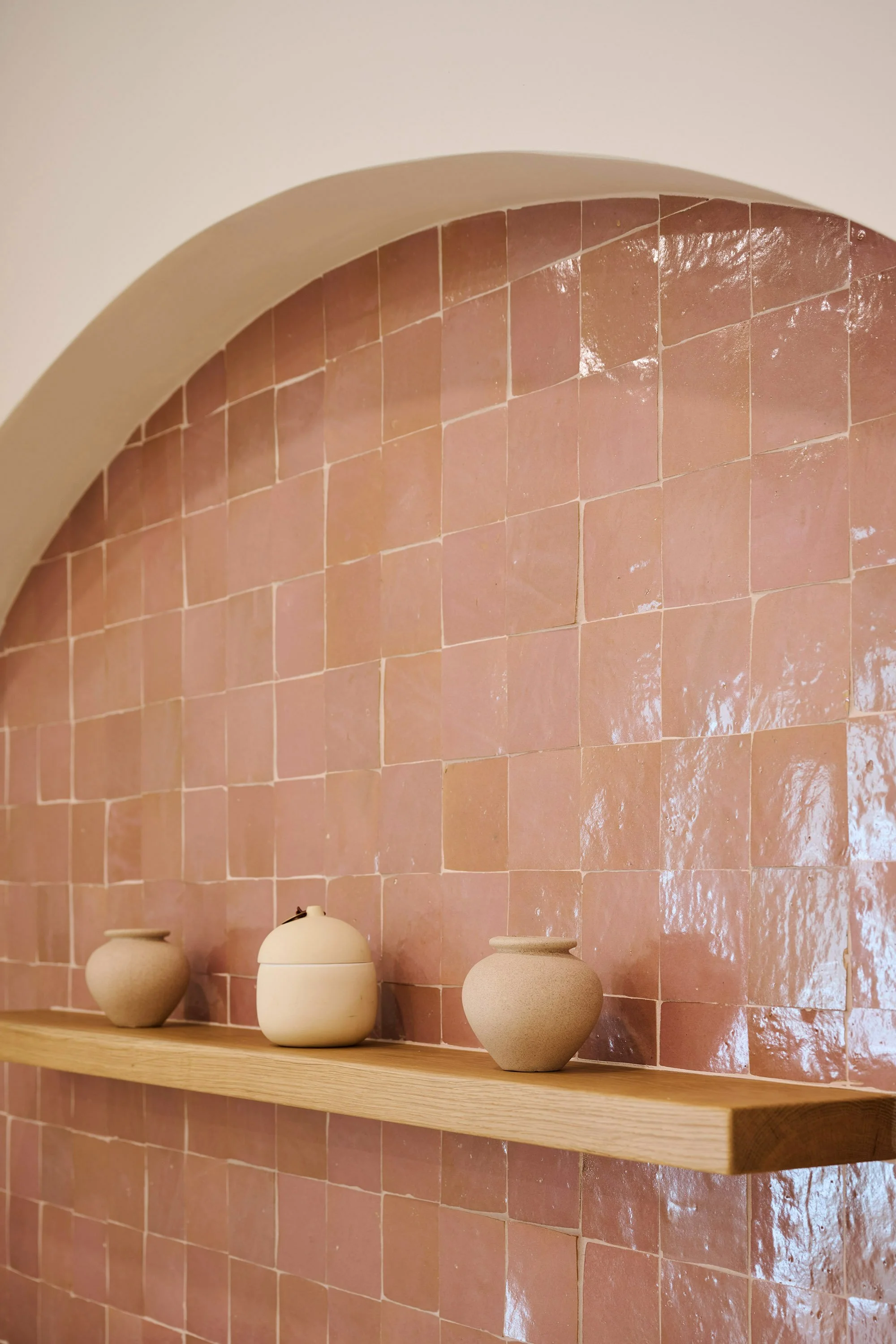 Decorative clay pots placed on a wooden shelf against a pink tiled wall with an arched ceiling.