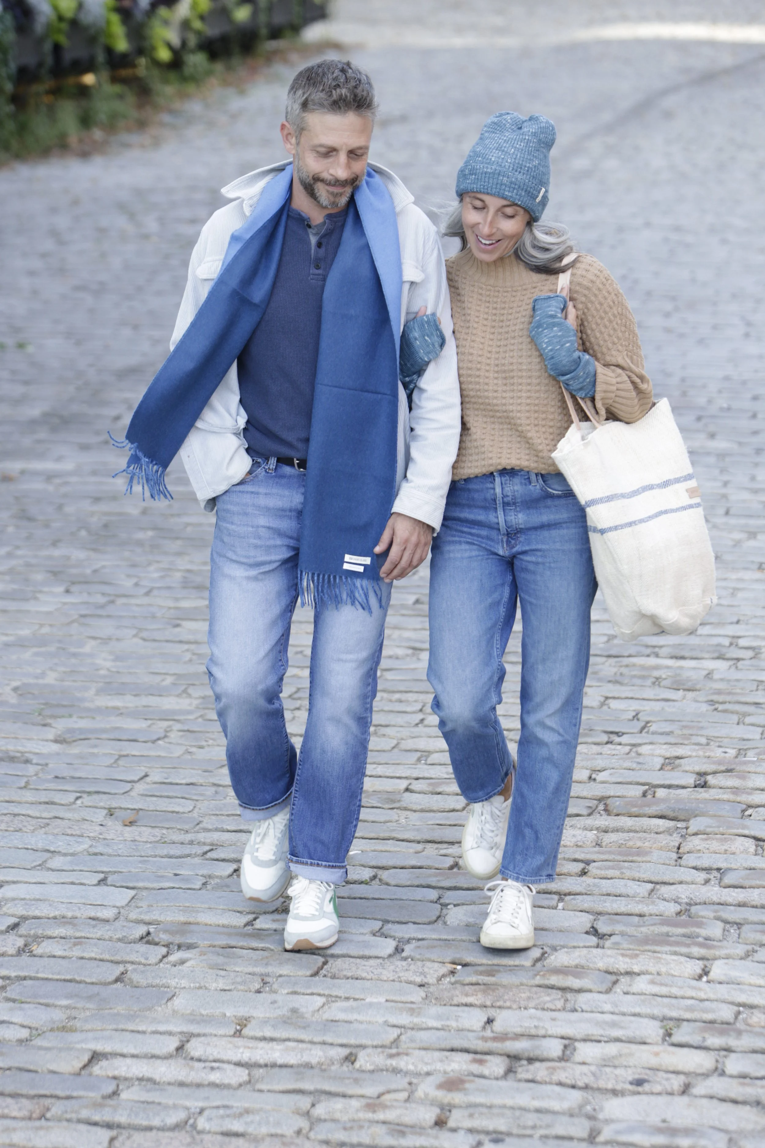 A middle-aged man and woman walking together on a cobblestone street, smiling and enjoying each other's company.