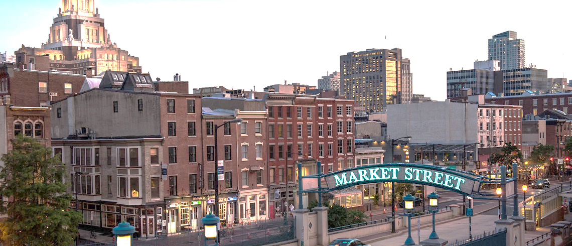 Cityscape of downtown with a 'Market Street' archway in the foreground and various buildings, including a tall church steeple, in the background at dusk.