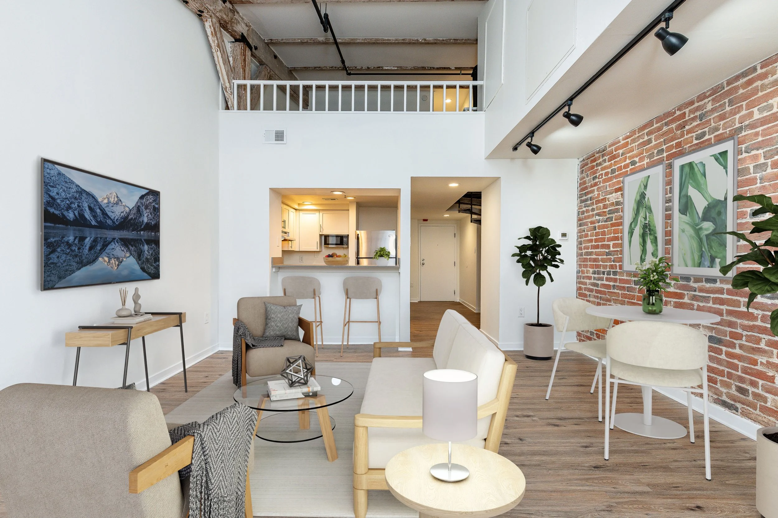 Open-concept living room with white walls, brick accent wall, modern furniture, wall art, potted plants, and a view into the kitchen.