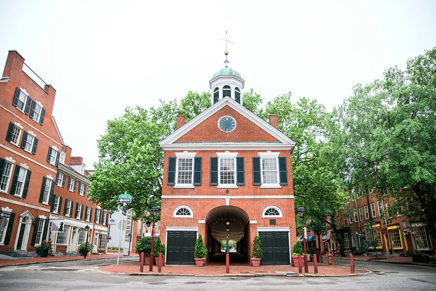 Historic brick building with clock and steeple, located on a city street, surrounded by trees and other brick buildings.