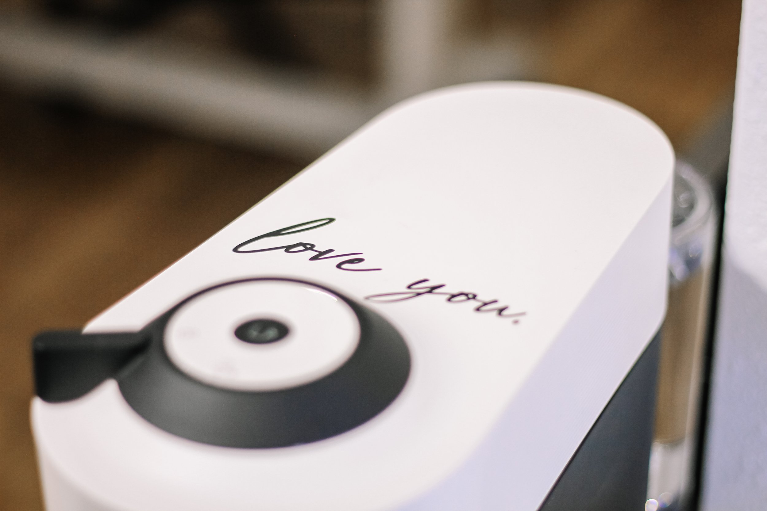 A white surface with black text reading 'Love you' and an illustration of a black and white camera lens.