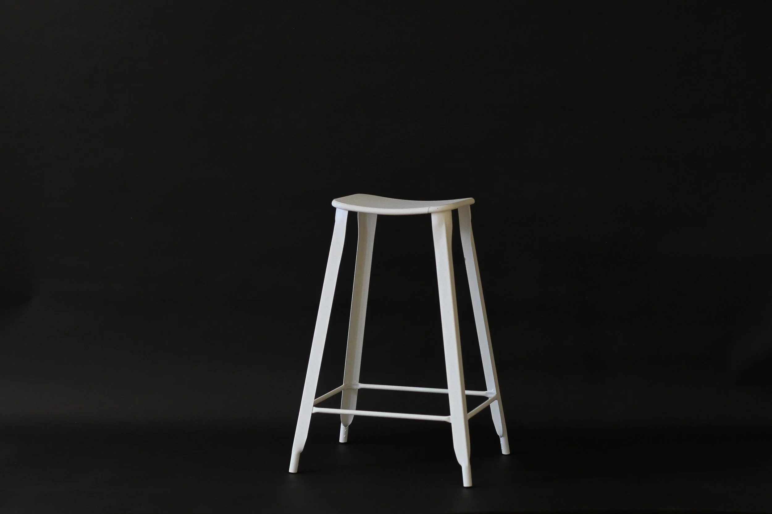 A white wooden stool with four legs and a curved seat against a black background.