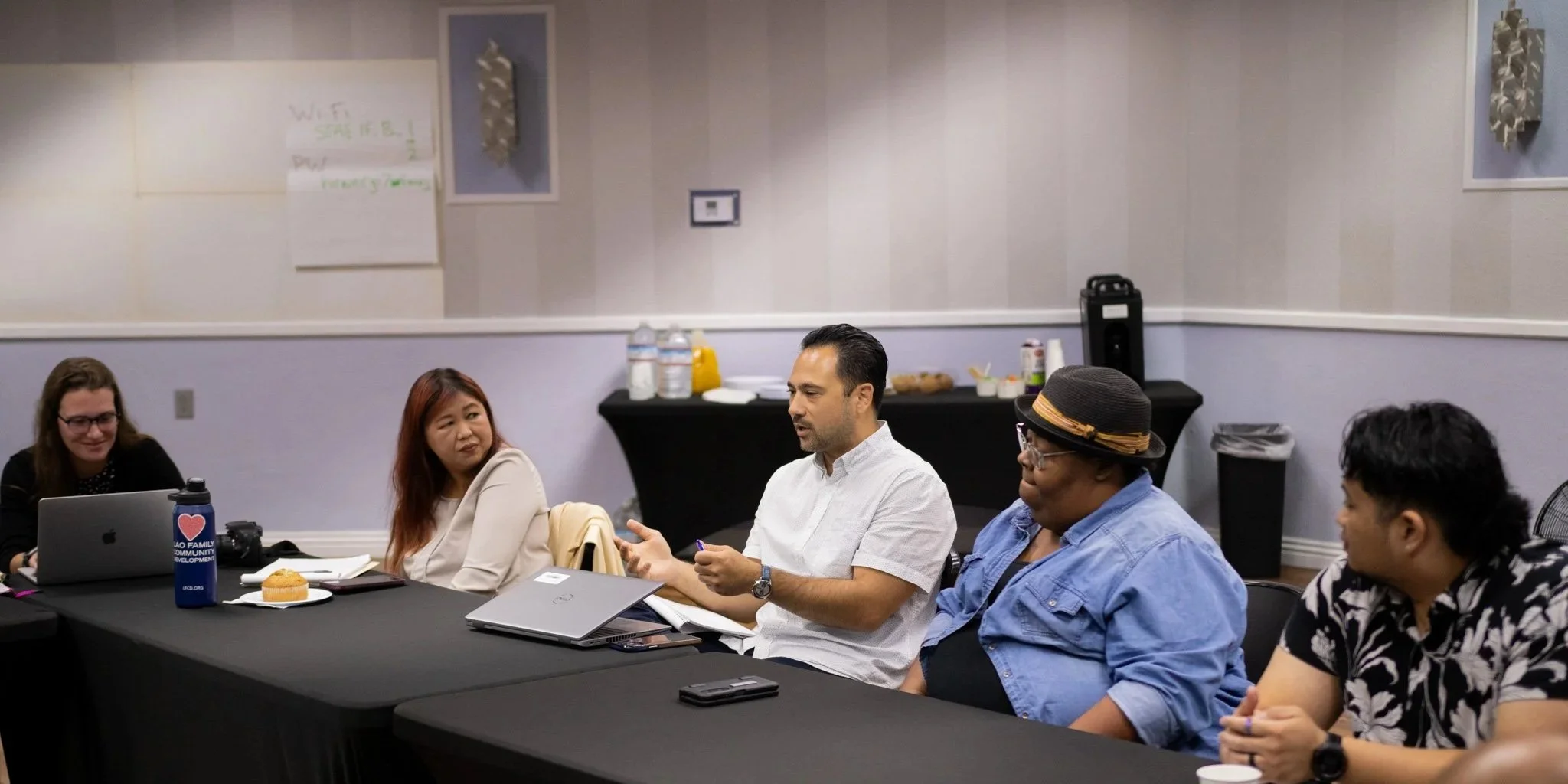 Group of people sitting around a rectangular table in a meeting room, engaged in discussion.