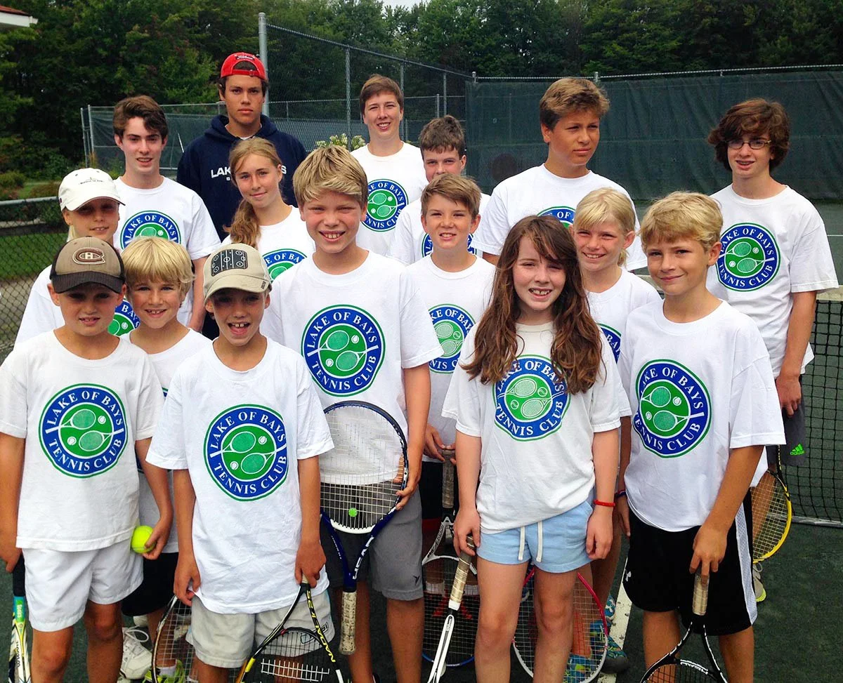 Group of children and teenagers posing on a tennis court, wearing 'Lake of Bays Tennis Club' T-shirts, holding tennis rackets and a tennis ball.