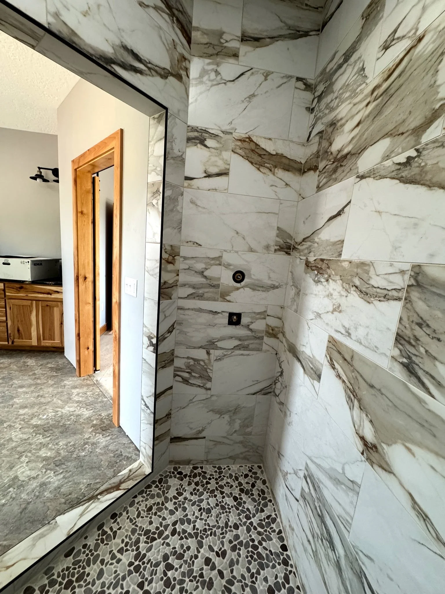 Double vanity bathroom with two mirrors, sinks, granite countertop, and tiled backsplash. Wall-mounted towel rings near each mirror, and a textured light-colored wall with lighting above.