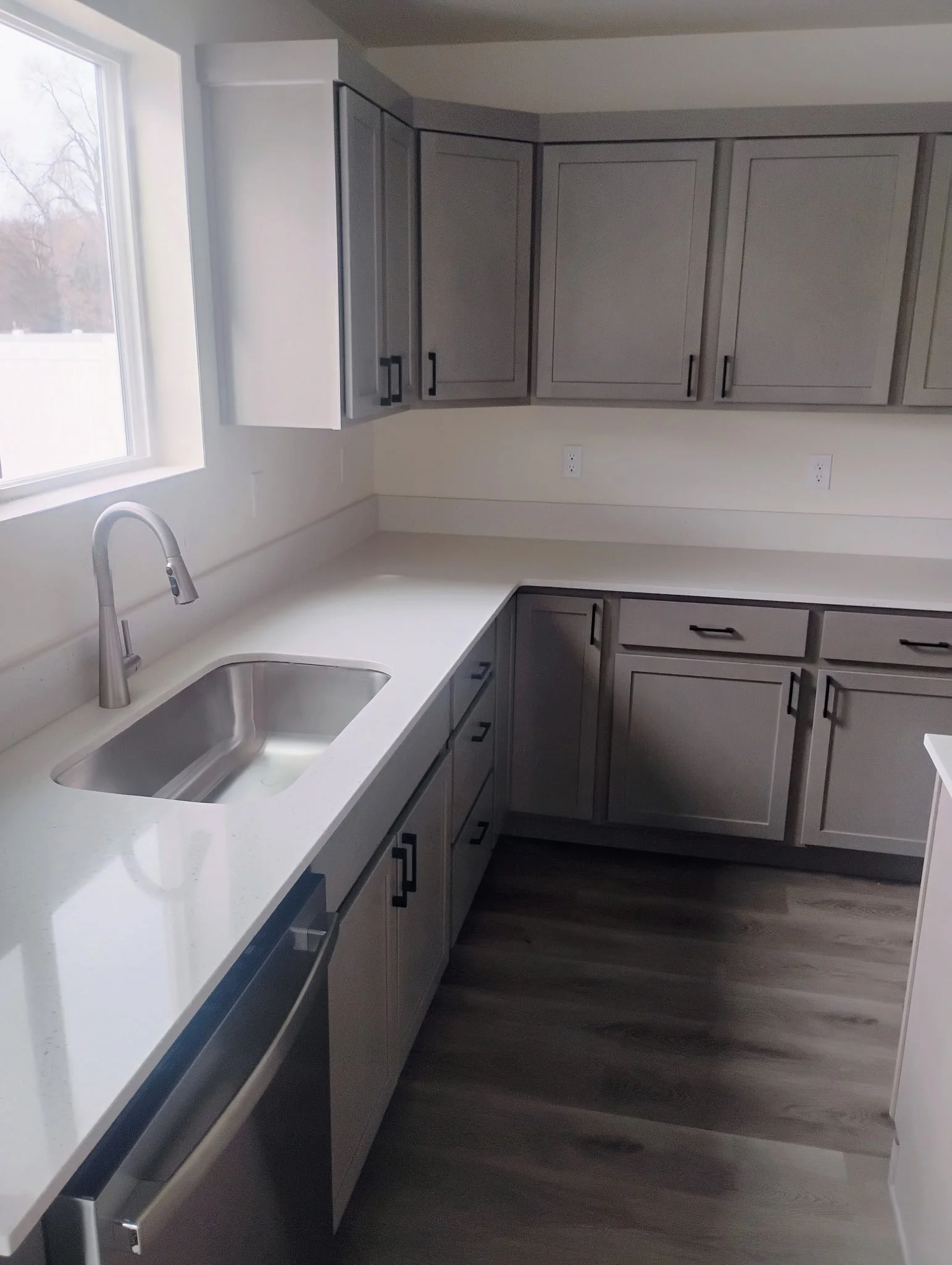 Modern kitchen with gray cabinets, white countertop, stainless steel sink, and window with outdoor view.