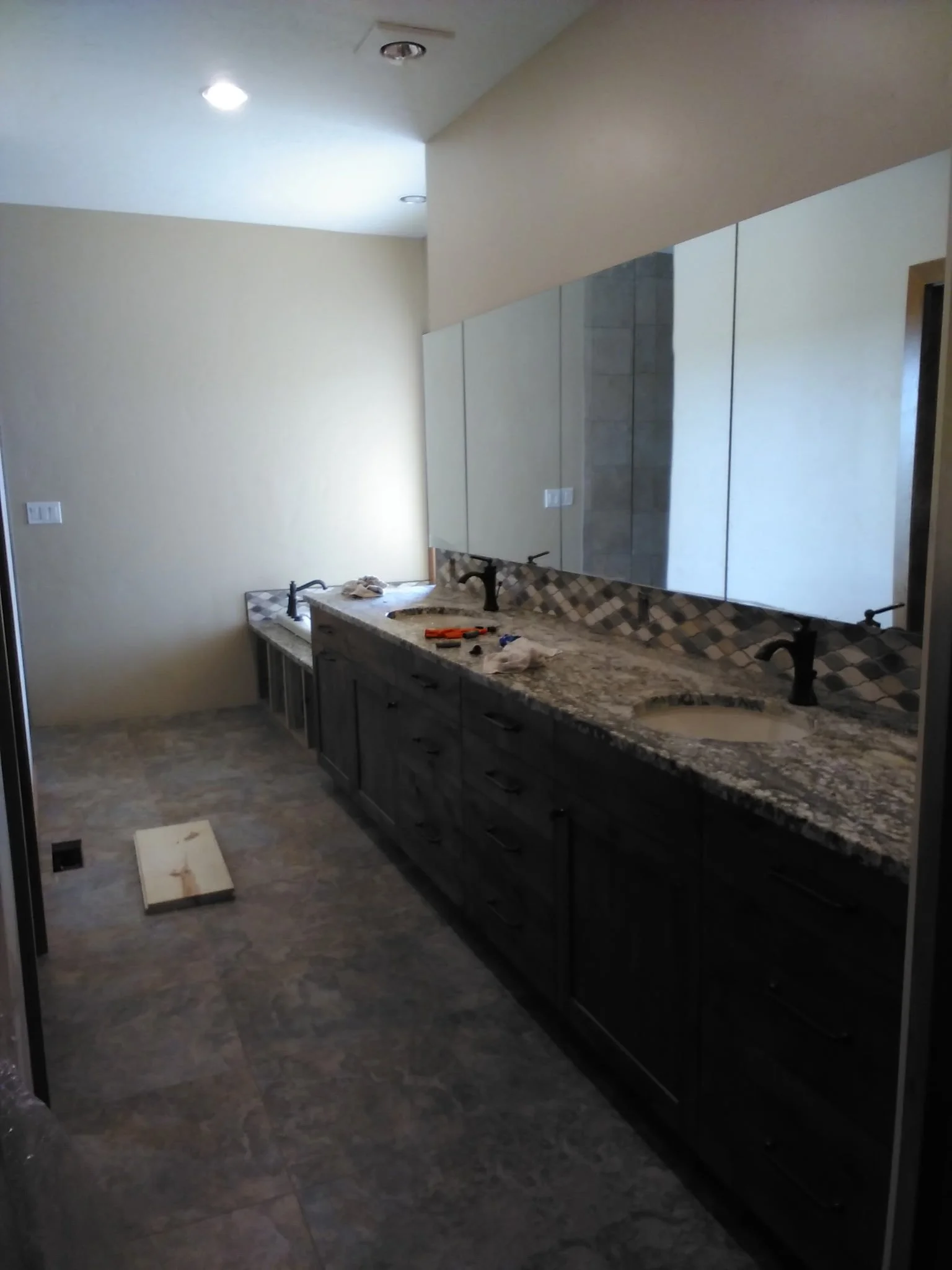 Bathroom under renovation with dark cabinetry, granite countertop, and a large mirror; items such as tools and towels on the counter, unfinished details, and construction materials visible.