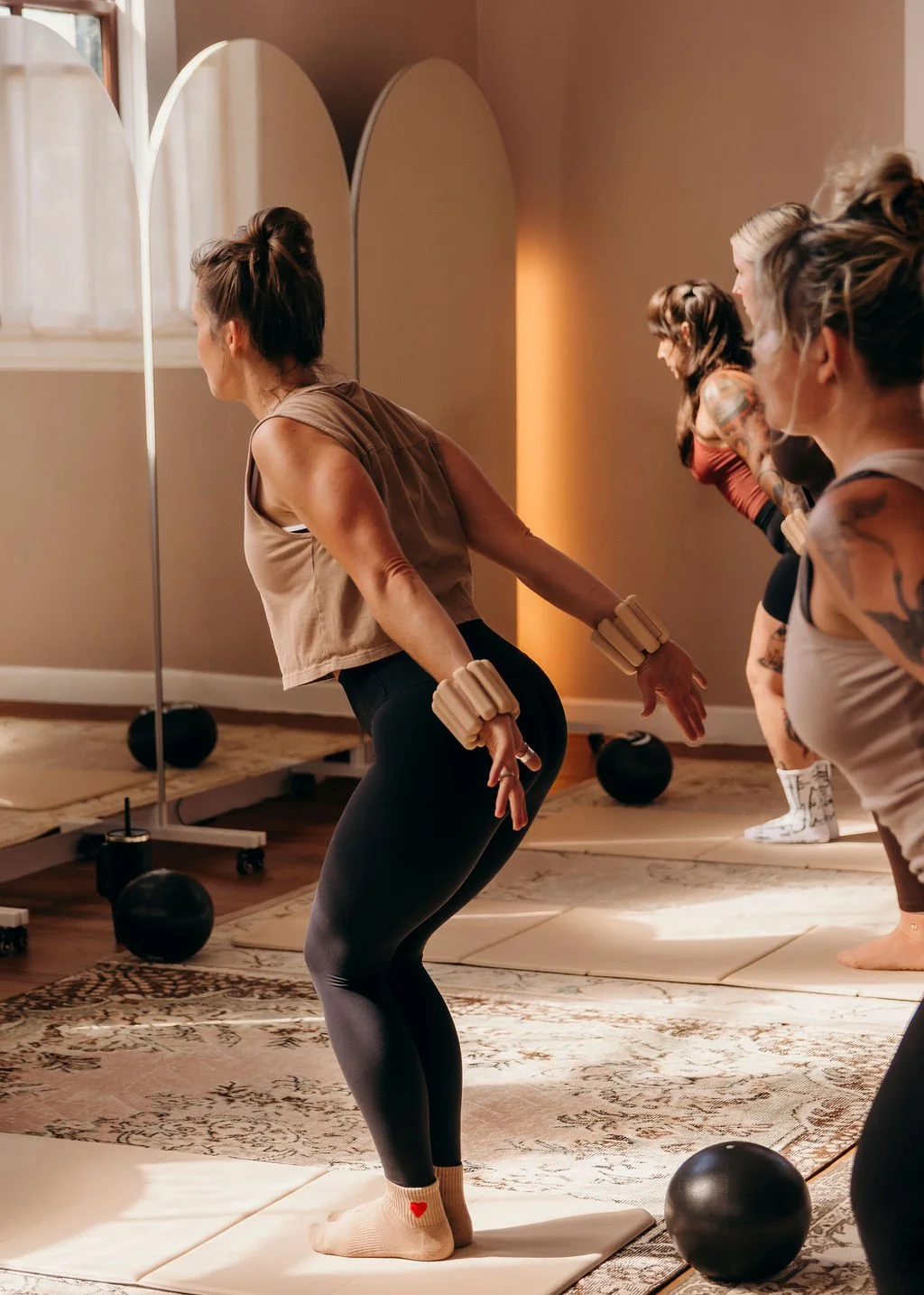 Women participating in a fitness class doing weight lifting exercises in a studio with mirrors and fitness equipment.