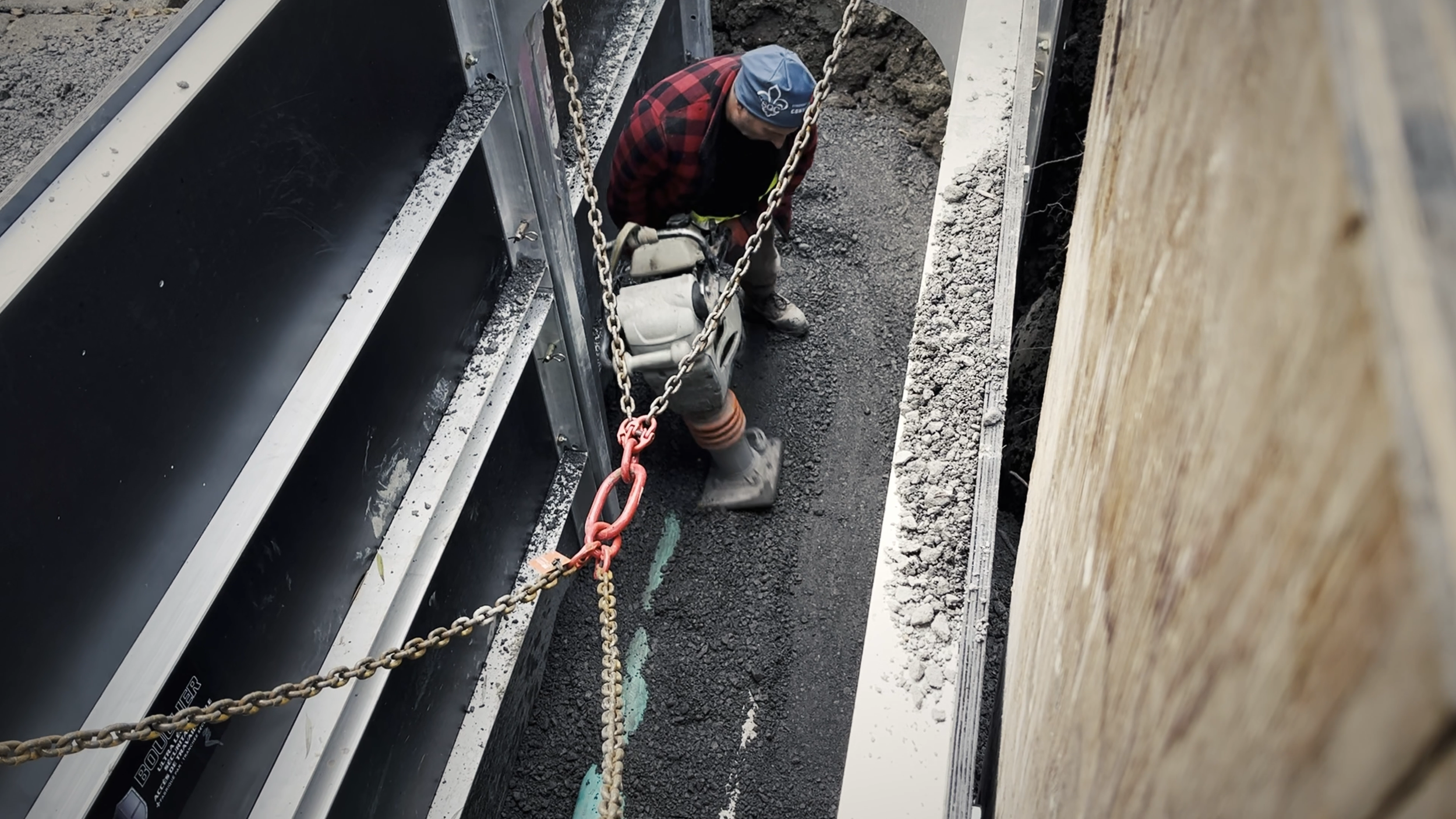 Un ouvrier utilisant une machine pour compacter ou niveler le bitume sur une surface de route en construction, entouré de chaînes de sécurité