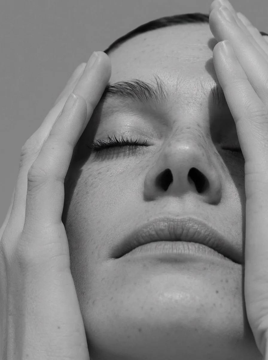 Close-up of a woman with eyes closed and hands on her face, in black and white.