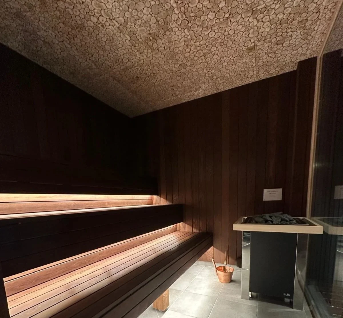 Sauna room with wooden benches, a bucket with a ladle, and a heater with rocks on top.