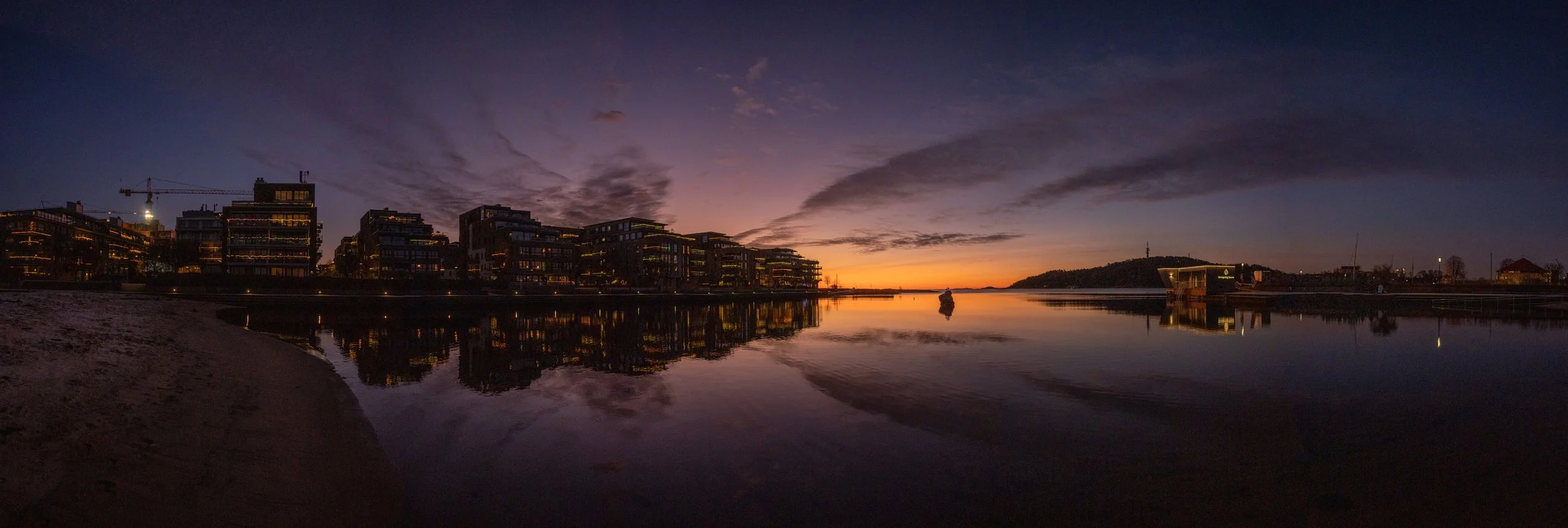 Cityscape at sunset with modern buildings reflected in calm water and dark clouds in the sky