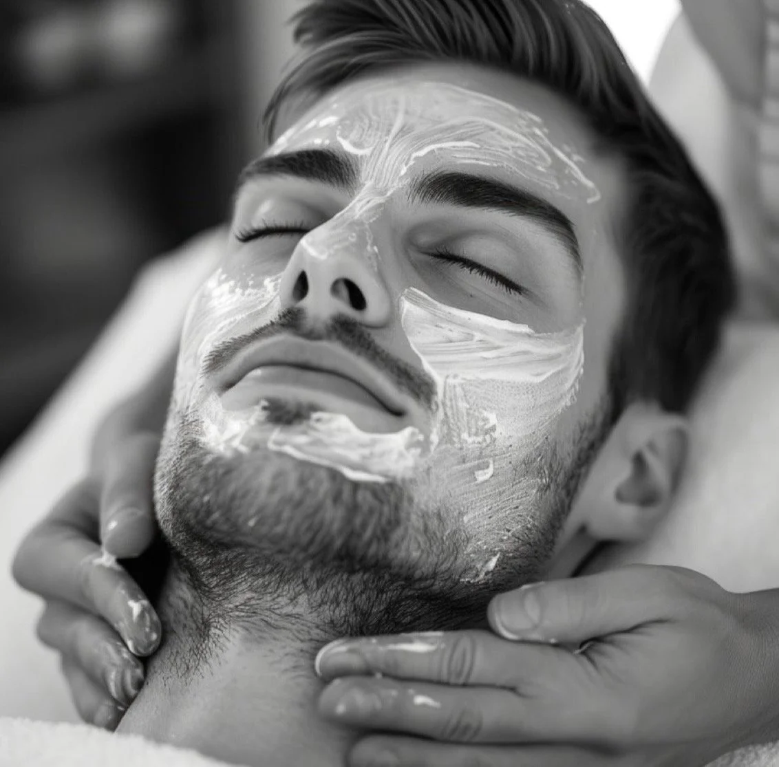 A man receiving a facial treatment, with a cream applied to his face, lying down with eyes closed.