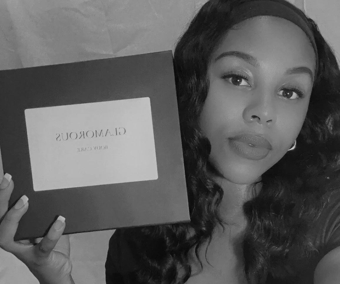 A woman with wavy hair holding a Clamorous Beauty box facing the camera.