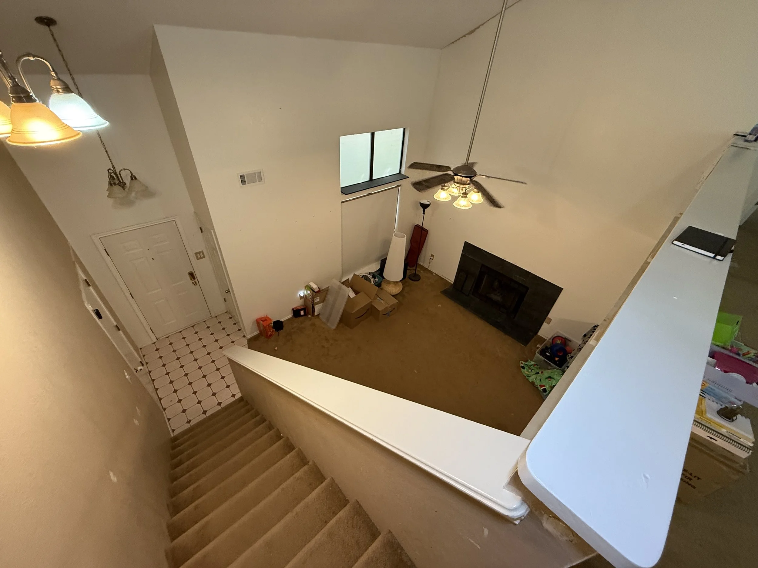 View of a living room from the top of staircase, showing the entry door, a floor lamp, a fireplace, and clutter including boxes and household items.