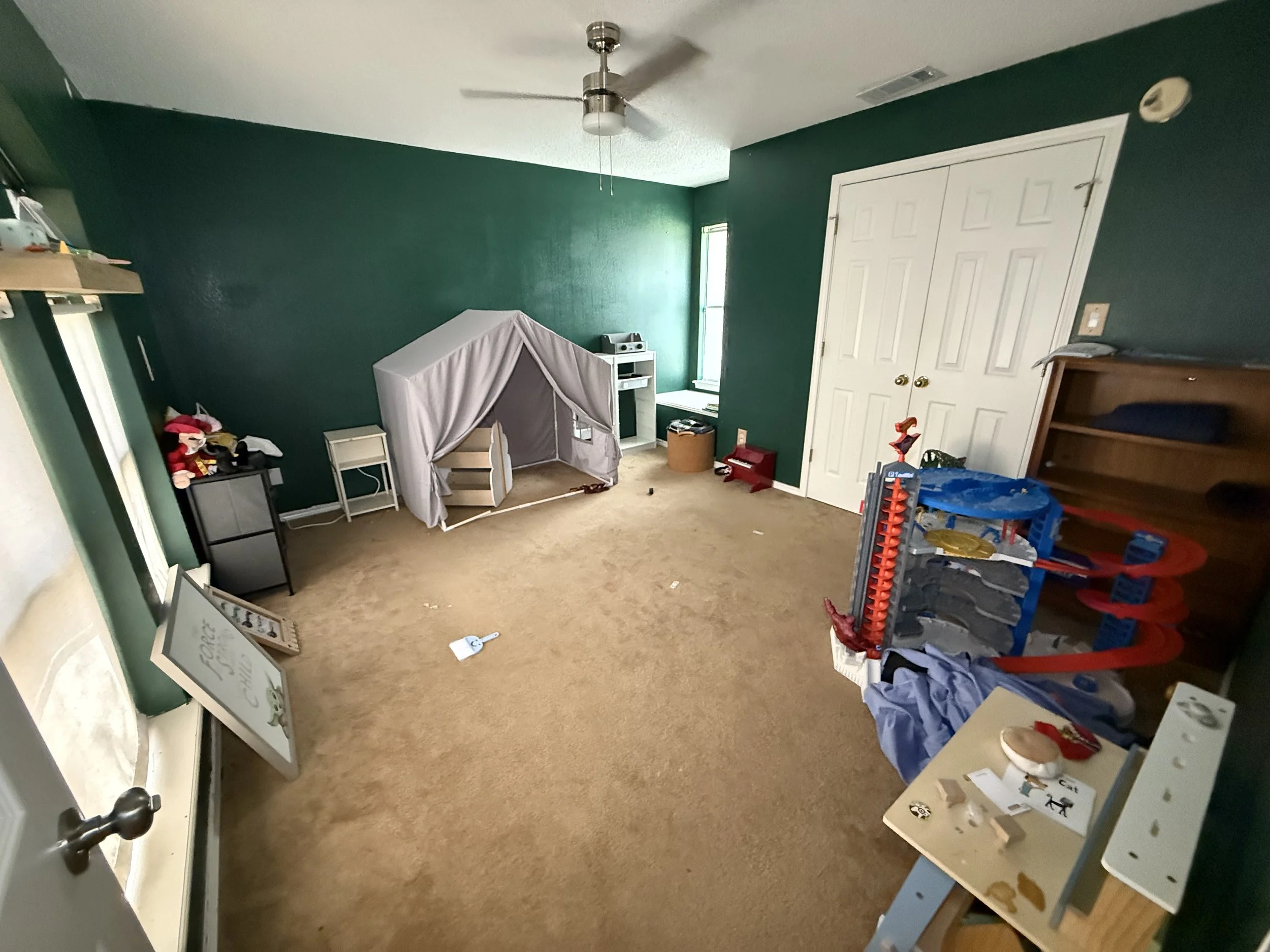 Child's playroom with green walls, beige carpet, a small tent, toy cars, and toys scattered around.
