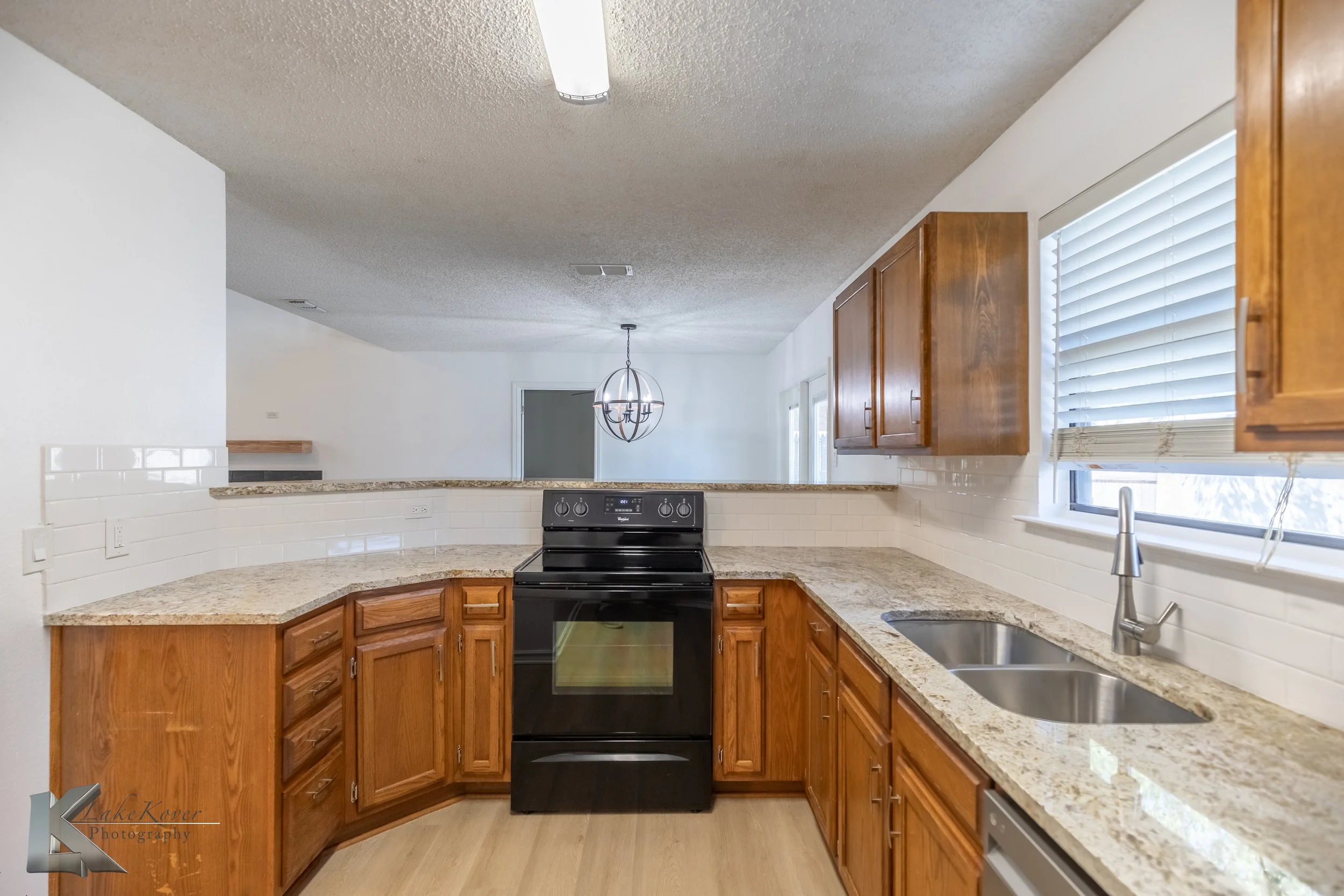 Kitchen with granite countertops, wooden cabinets, a black stove, and a double sink with a window above it.