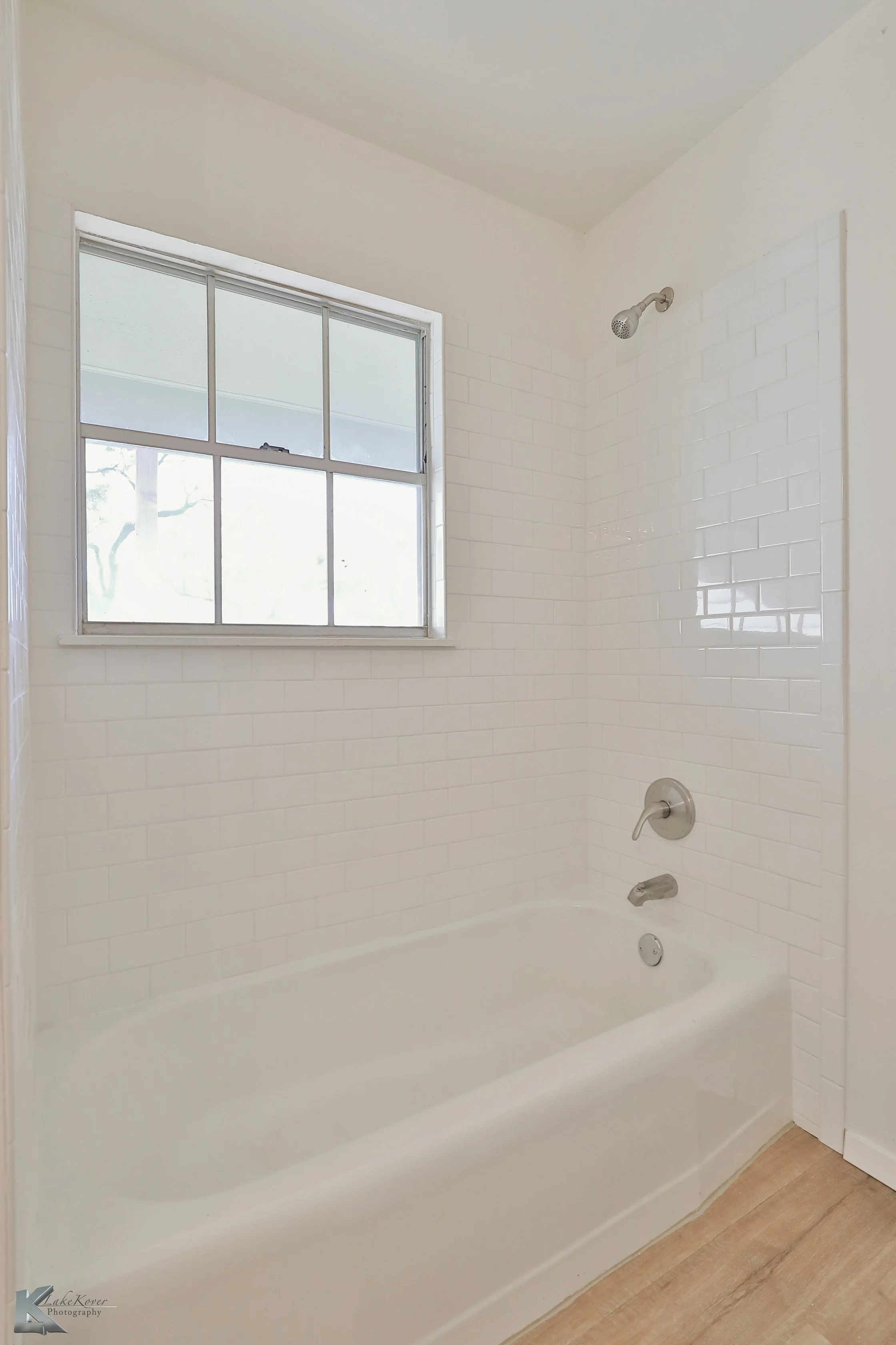 A bathroom with a bathtub, a window above the tub, and white tiled walls.