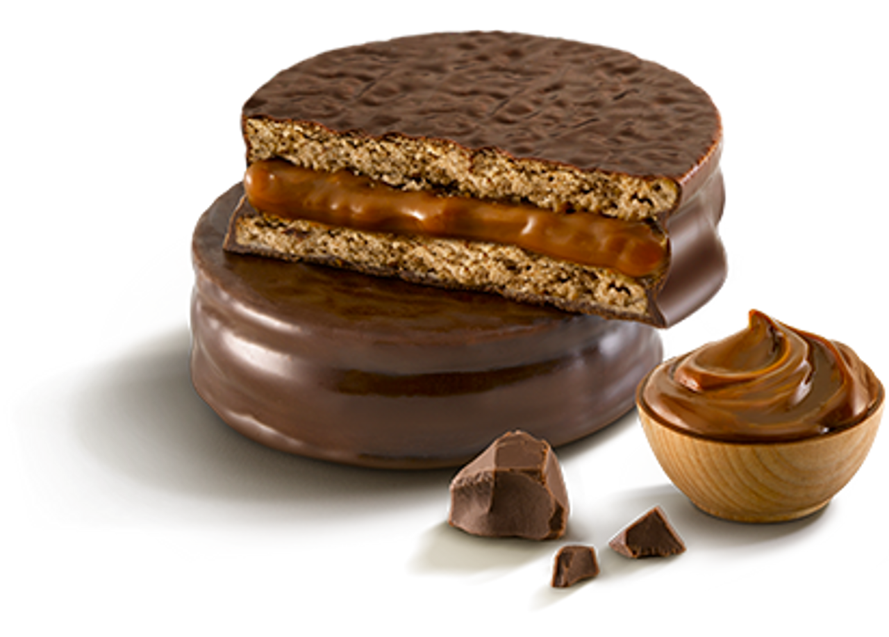 Chocolate cake with a layer of caramel and cookies inside, topped with a chocolate glaze, accompanied by a bowl of caramel sauce and pieces of chocolate.