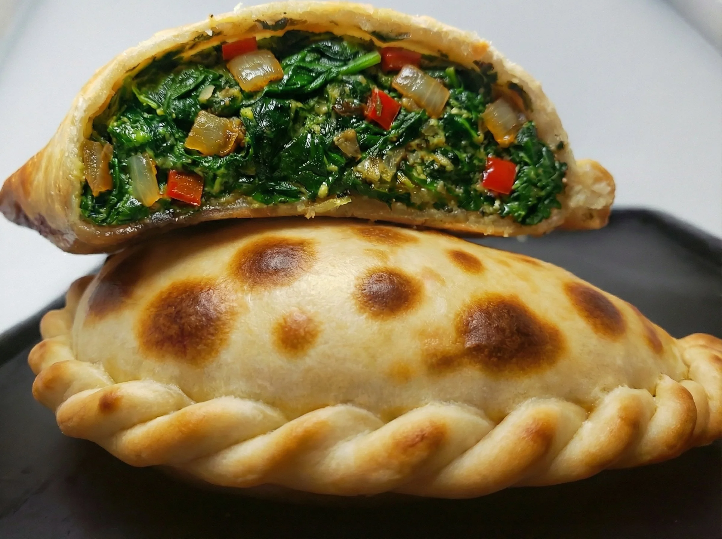 A baked empanada with a golden brown, braided crust, sliced open to reveal a filling of cooked greens and diced vegetables.