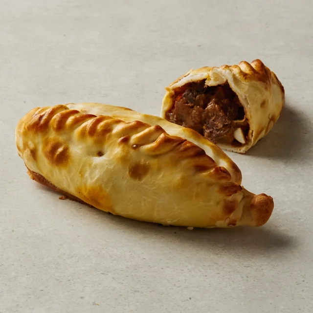 Two golden-brown breaded and baked pastry pockets, one whole and one cut in half showing a meat filling inside, resting on a light gray surface.