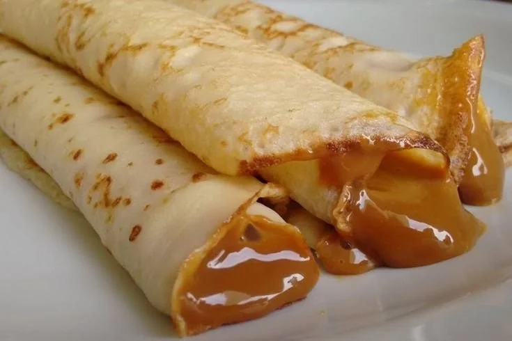 Two crepes filled with caramel sauce on a white plate.