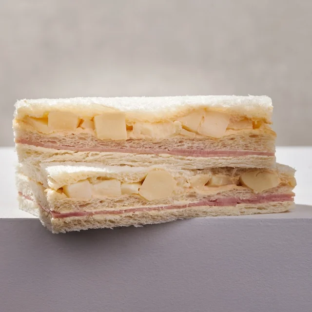 Close-up of a white layered sandwich with ham, cheese, and bread, cut in half to show inside.