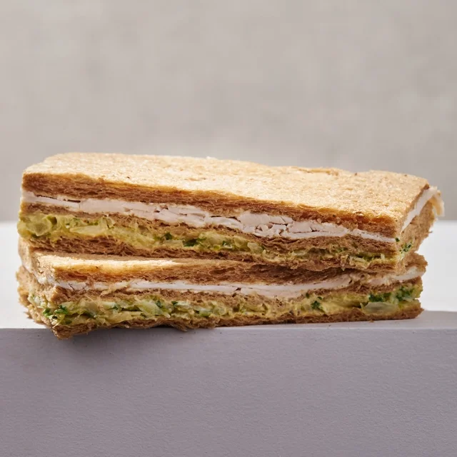 Half of a club sandwich with turkey, lettuce, and bread slices on a gray surface.