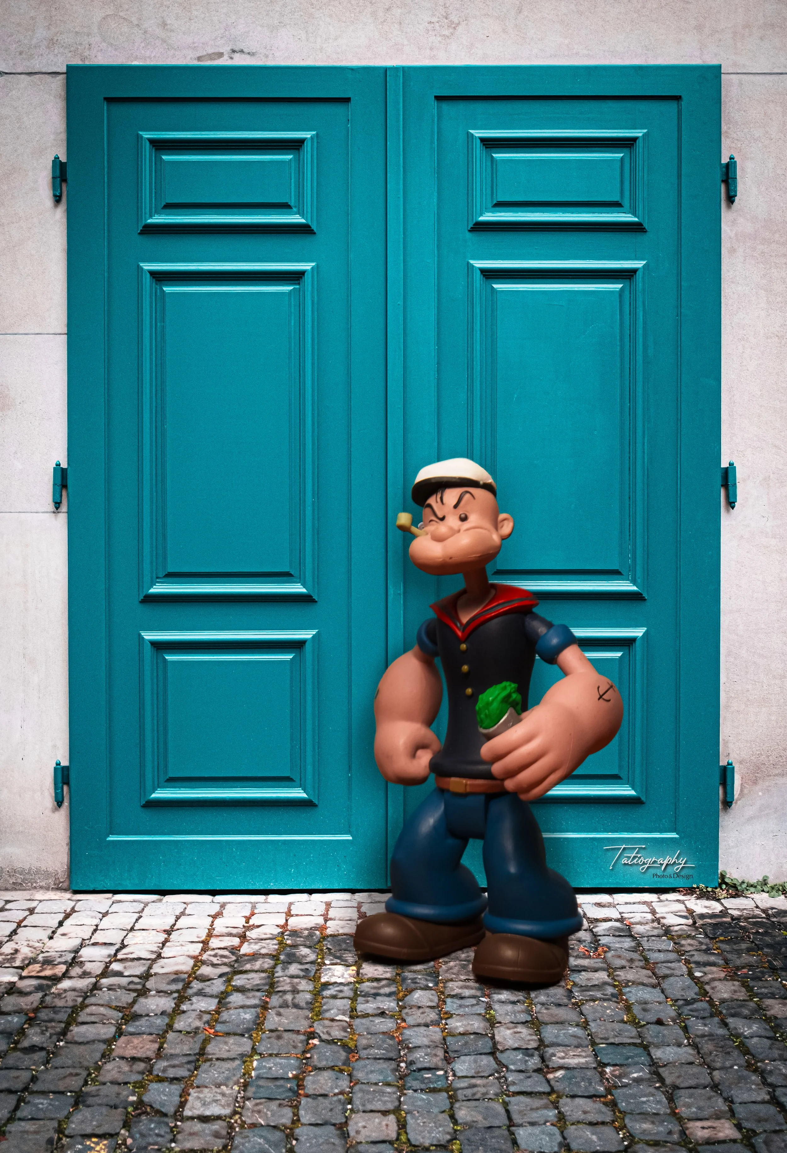 A statue of Tintin, the comic book character, standing in front of teal double doors, with cobblestone pavement underneath.