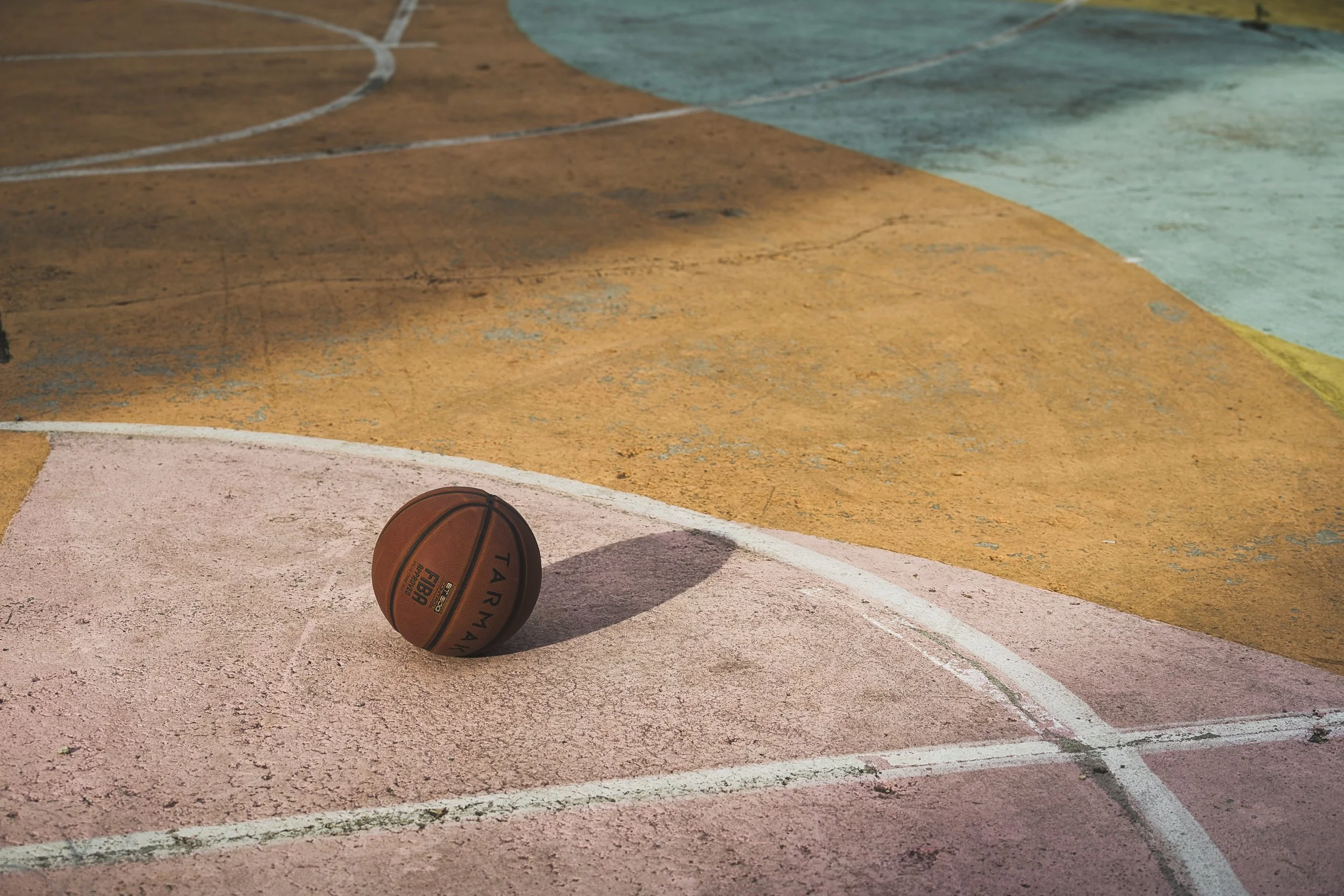 An old basketball on a colorful, worn outdoor basketball court with faded lines and textures.