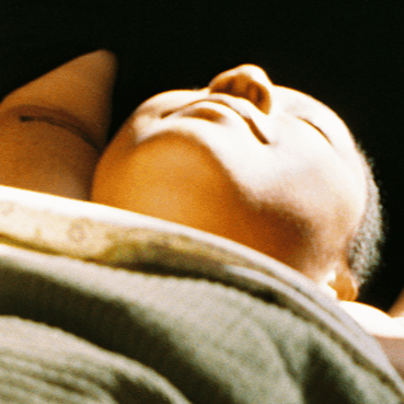 Close-up of a sleeping baby with a peaceful expression, resting with their head slightly tilted back.